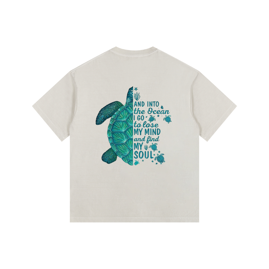 An off-white  TOTZ WORLD short-sleeve t-shirt with a graphic on the back featuring a teal sea turtle and the text 'AND INTO the Ocean I GO to lose MY MIND and find MY SOUL' in teal lettering, set against a plain white background.