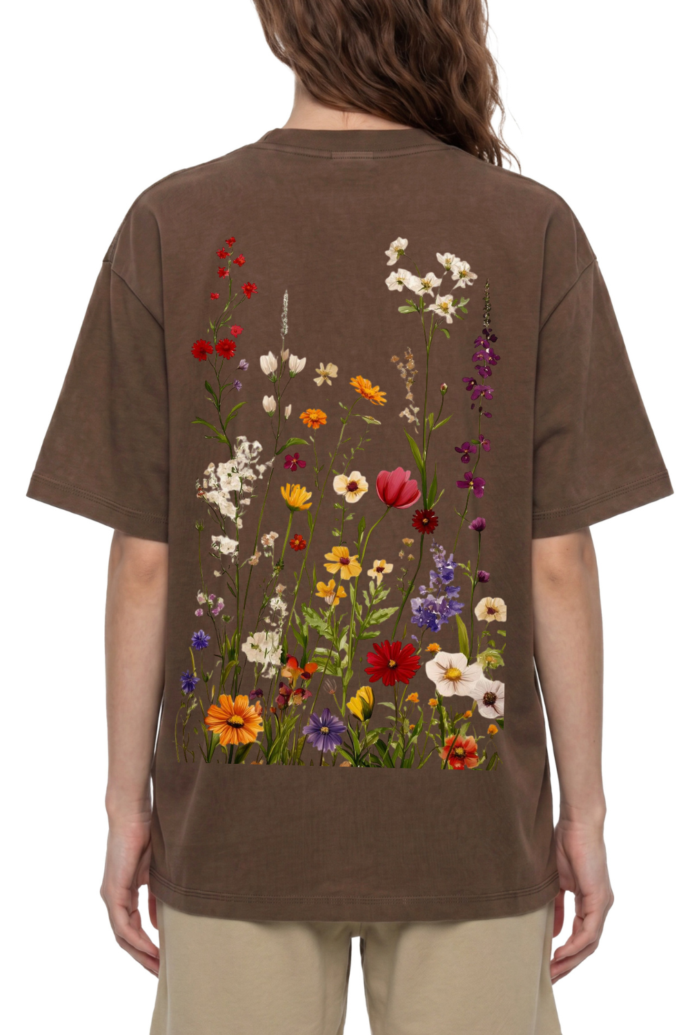 A person viewed from the back wearing an oversized brown T-shirt with a large multicolor wildflower print across the back, paired with light beige pants, against a plain white background.