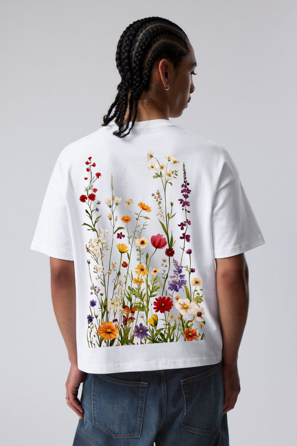 A man viewed from behind wearing a white short-sleeve t-shirt with a large, colorful wildflower print on the back, paired with blue jeans against a light gray studio background.